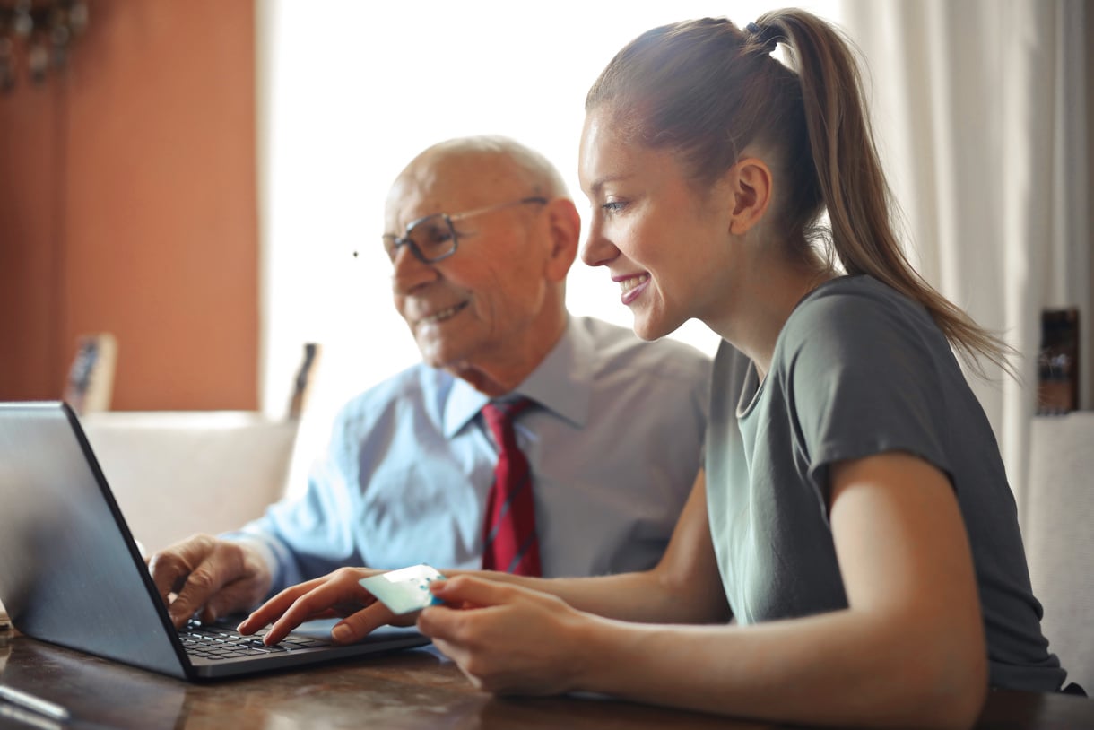 Young woman helping senior man with payment on Internet using laptop